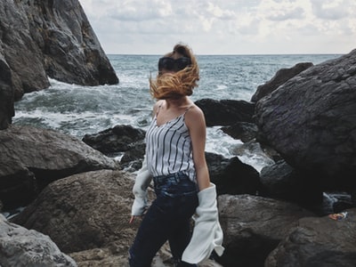 女人穿着白色背心和蓝色牛仔裤站在岩石海岸白天
